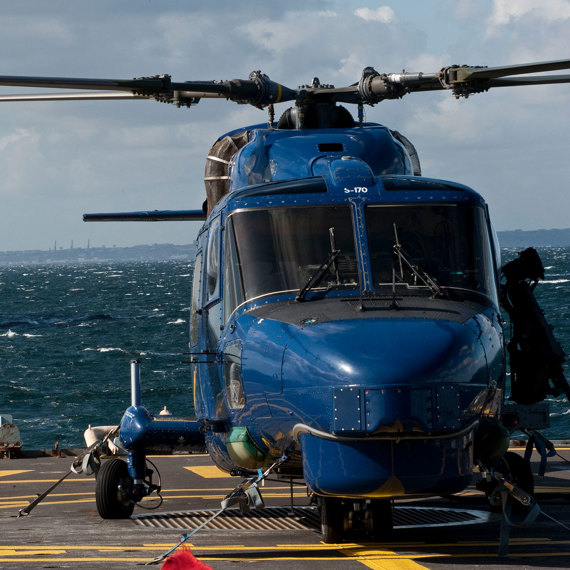 Blue helicopter on a ship's deck with a naval ship approaching.