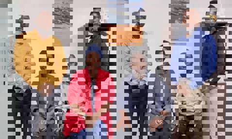 四个人在办公室里摆姿势，墙上挂着一张DESMI海报。