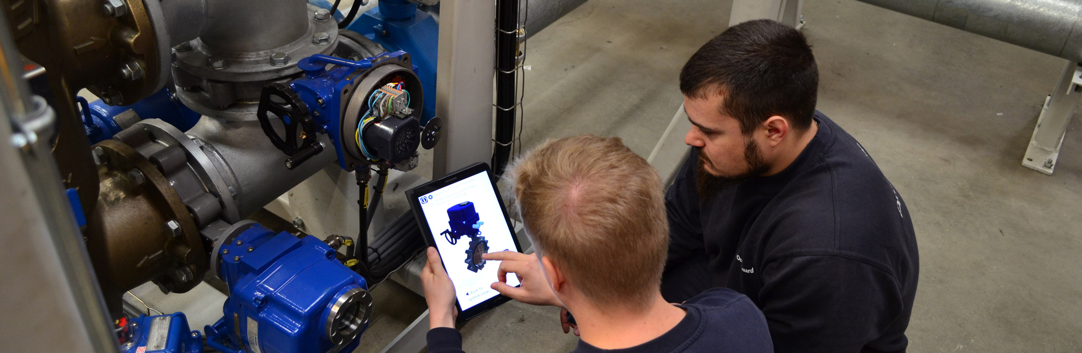 Two technicians inspect DESMI equipment using a tablet for fluid handling.