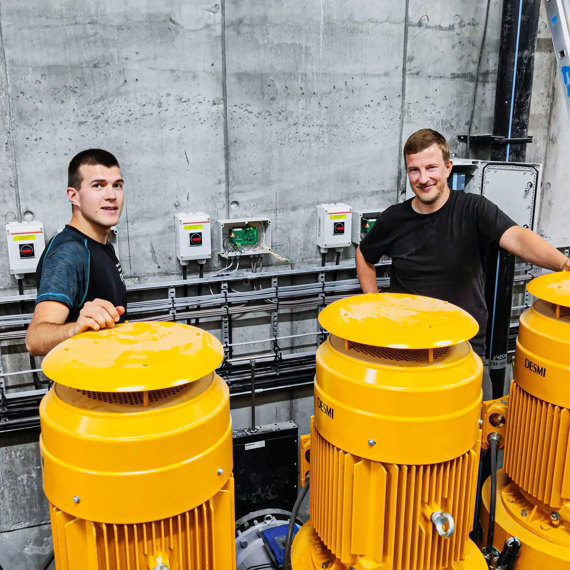 Two men stand by DESMI pumps in an industrial setting.