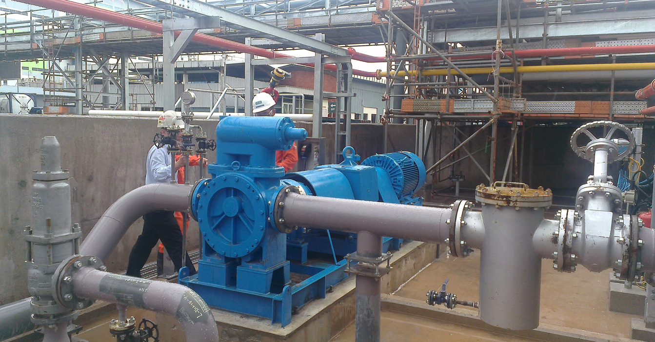 Industrial setting with blue pump and workers inspecting pipework and equipment.