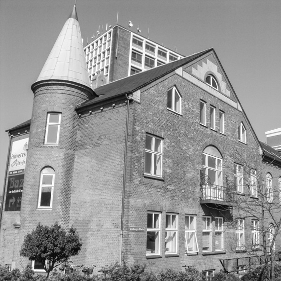Historic brick building with a turret, adjacent to modern structures, under clear sky.