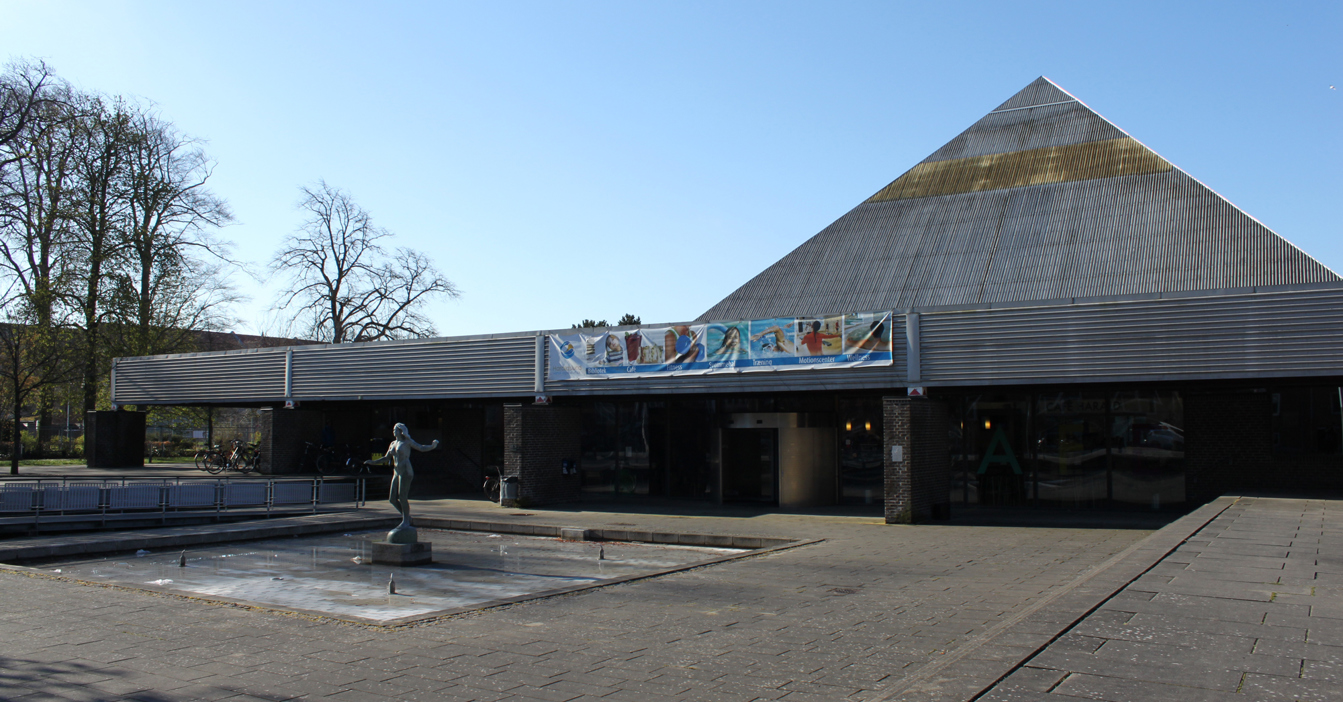 Modern building with a triangular roof, banner, and a statue in the foreground.