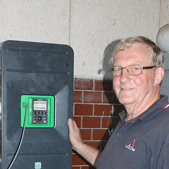 Man standing next to a mounted electronic device on a wall.