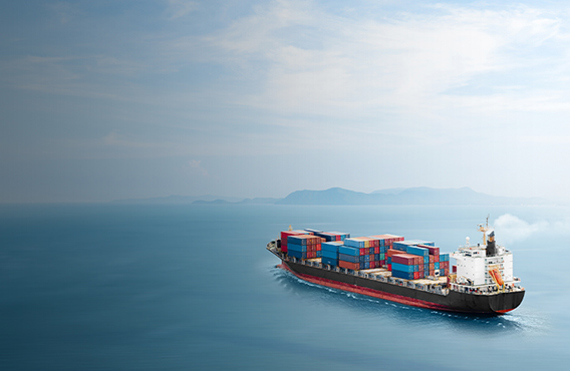 Cargo ship carrying containers on a calm ocean with distant islands visible.