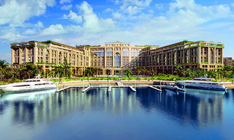 Luxurious waterfront hotel with yachts docked, surrounded by palm trees and blue skies.
