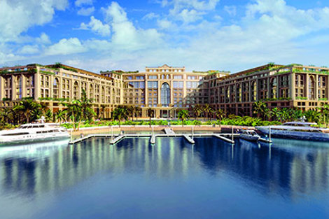 Luxurious waterfront hotel with yachts docked, surrounded by palm trees and blue skies.