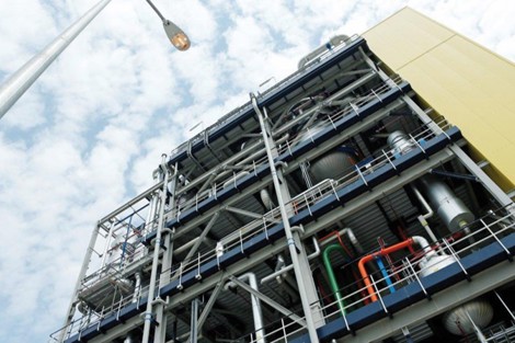 Industrial facility with complex piping and structures against a cloudy sky backdrop.
