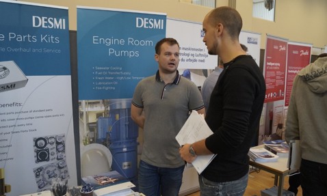 Two men discussing in front of DESMI engine room pumps display.