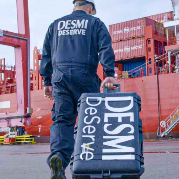 Arbetare i DESMI-uniform bär utrustningsväska vid en hamn.