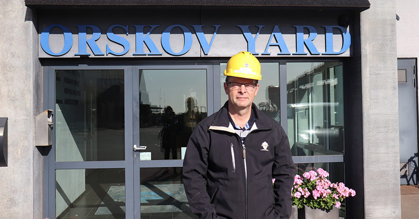 Man in a yellow hard hat stands in front of Orskov Yard entrance.