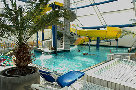 Indoor pool with a yellow slide, palm tree, and lounge chairs.