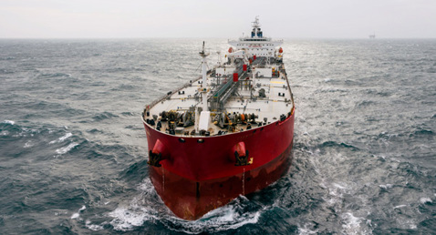 Large red cargo ship navigating through choppy ocean waters under an overcast sky.