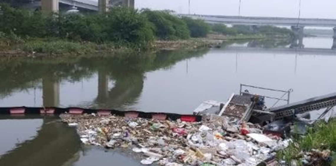 River with floating trash barrier under highway bridges.