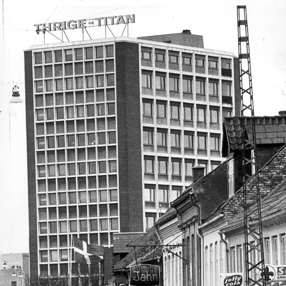 Street view with vintage cars, buildings, and "Thrigetitian" sign on high-rise.