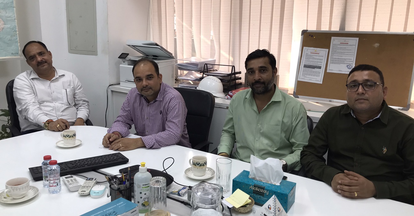 四名男子坐在会议桌旁，桌上有饮料和文件。