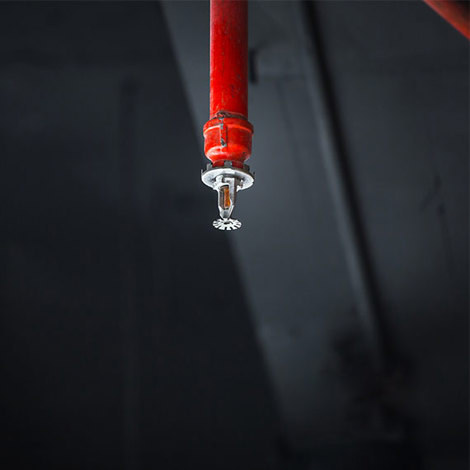 Red ceiling-mounted fire sprinkler against a dark background.