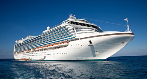 Large white cruise ship sailing on a clear blue ocean.