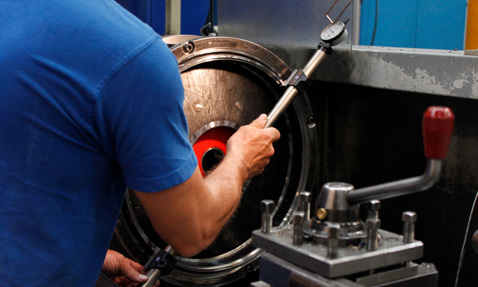Technician measuring a metal component with a gauge in an industrial setting.