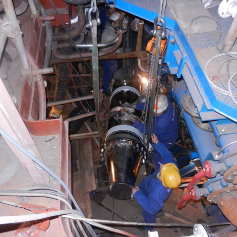 Workers installing equipment with chains in an industrial setting for fluid handling.