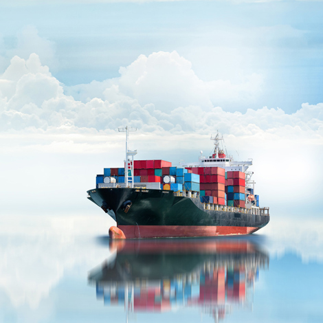 Cargo ship with colorful containers reflected on calm ocean water, under cloudy sky.