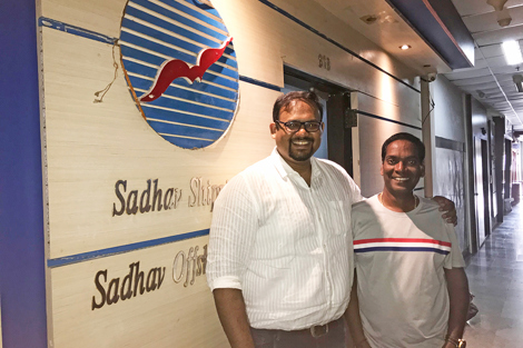 Two people smiling in front of Sadhav Shipping office sign.