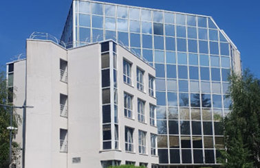 Modern glass office building with adjacent white structure, surrounded by greenery.