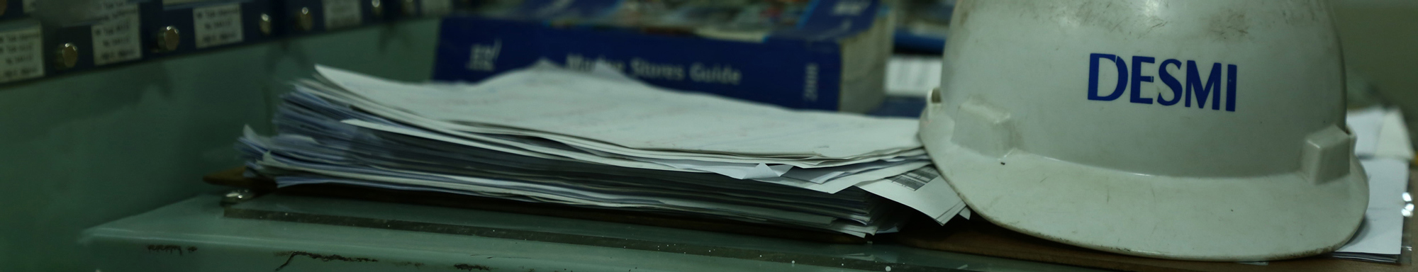 DESMI hard hat and stack of papers on a desk in an industrial setting.