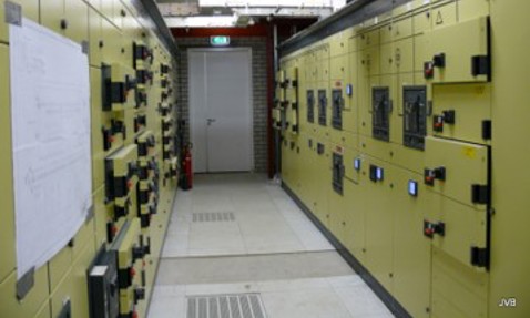 Industrial control room with yellow electrical panels and safety equipment.