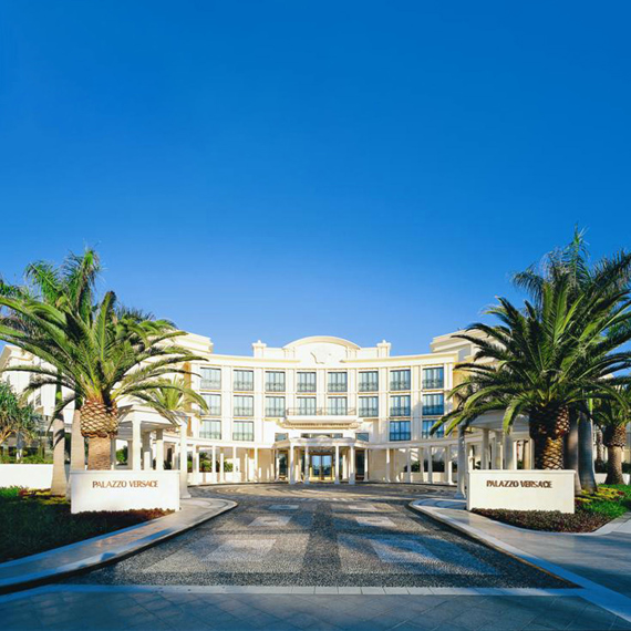 Luxury hotel entrance with palm trees and a clear blue sky.