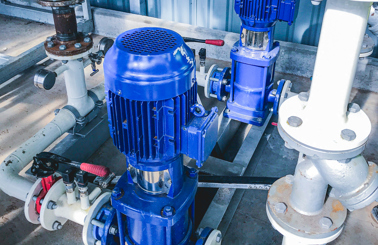 Blue industrial pumps connected to white pipes in a facility setting.
