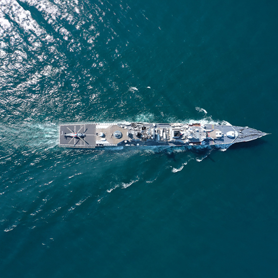 Aerial view of a naval ship sailing in clear blue ocean waters.