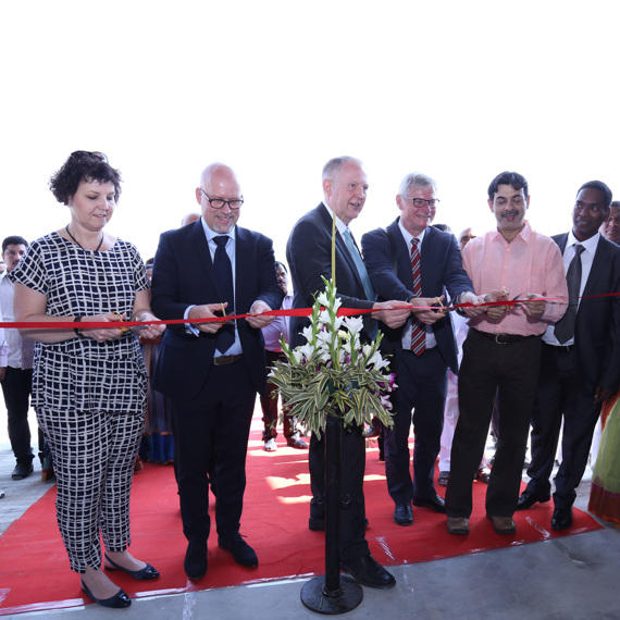 Group of people cutting a red ribbon at an event opening.