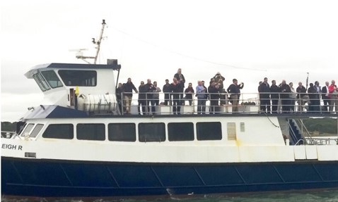 People standing on a ferry deck over water, with cloudy sky background.