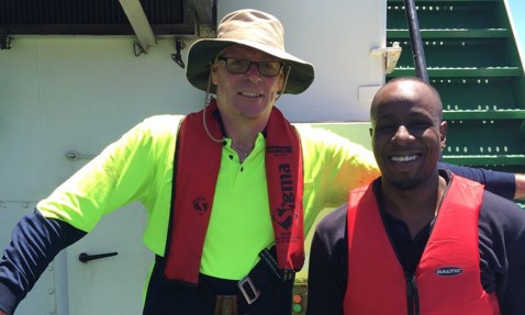 Two men wearing life jackets standing on a ship deck, smiling.