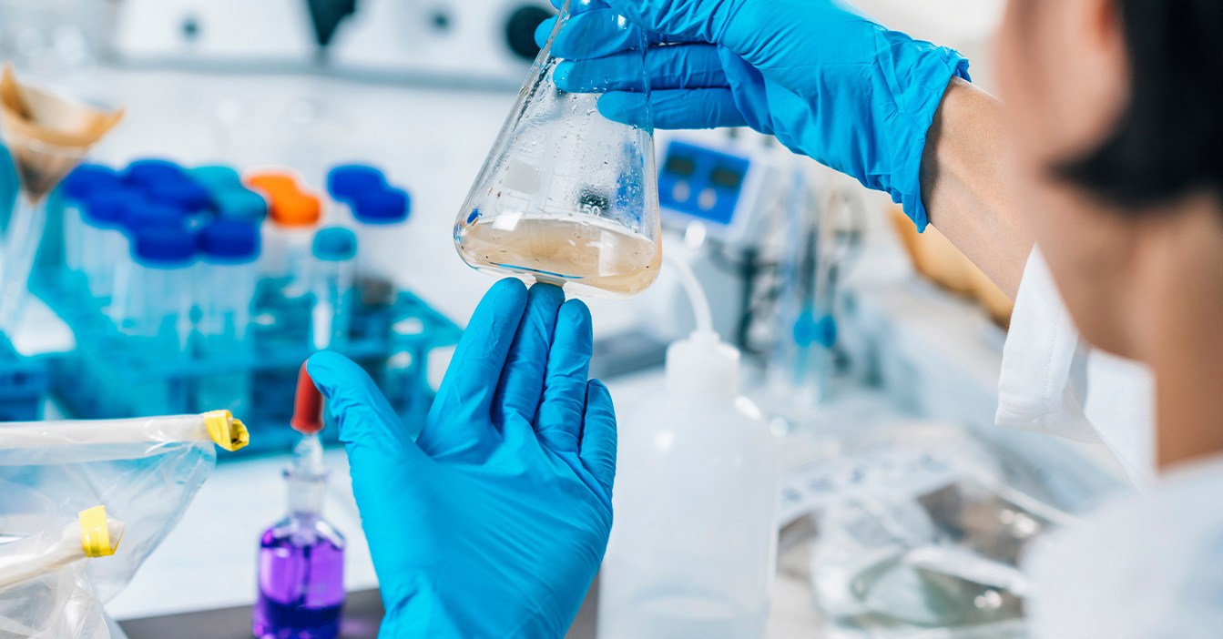 Scientist wearing blue gloves examines a flask in a laboratory setting.