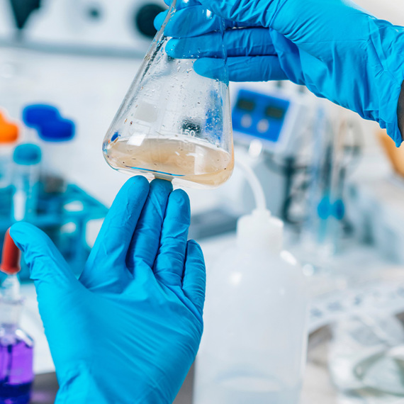 Scientist wearing blue gloves examines a flask in a laboratory setting.