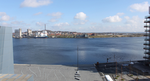 Riverside cityscape with industrial buildings and a bus on the road.