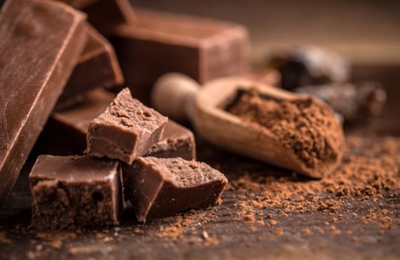 Chunks of chocolate and cocoa powder with a wooden scoop on a table.