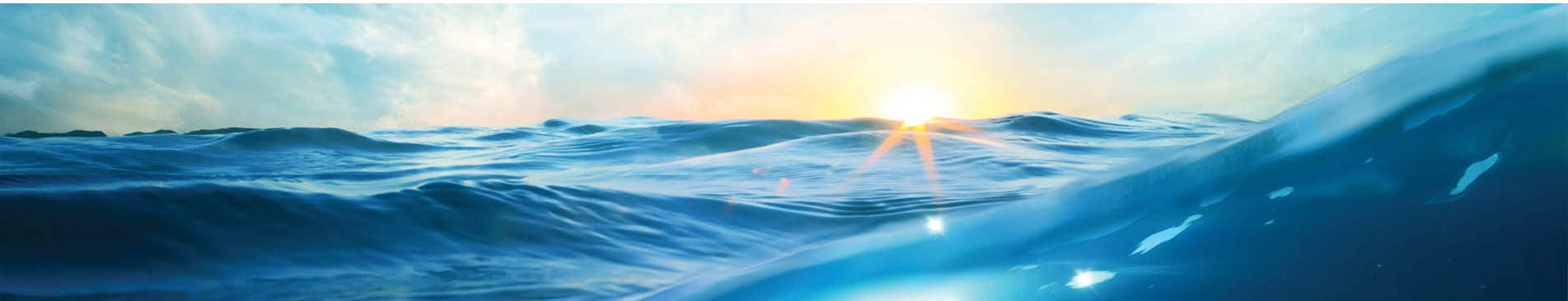 Sunrise over a calm ocean with gentle waves and a bright sky.