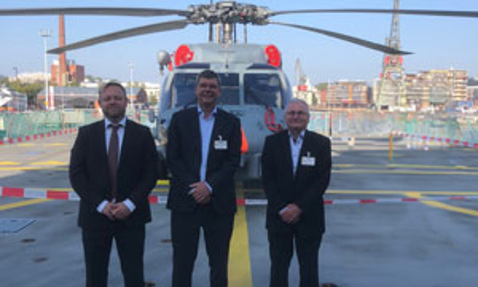 Three men in suits standing in front of a helicopter on a helipad.