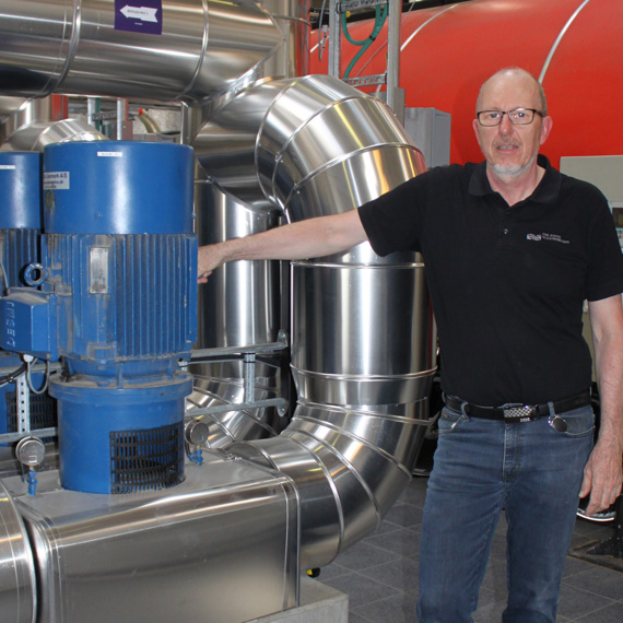 一名男子站在设施内的工业泵和管道旁。