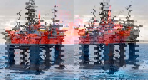 Offshore oil rig platform in the ocean, with waves crashing against its structure.