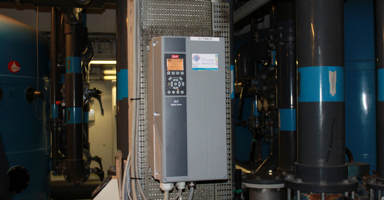 Industrial control panel with VLT AQUA Drive in a mechanical room setting.