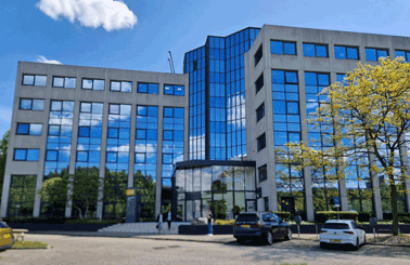 Modern office building with reflective glass facade and parked cars outside.