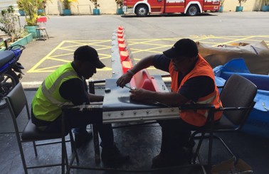 Two workers assembling equipment outdoors near a fire truck.
