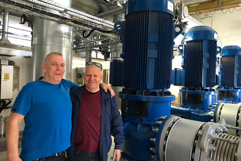 Two men standing in an industrial setting with large blue pumps.