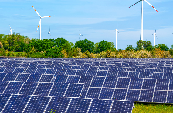 Solar panels and wind turbines in a green landscape under a clear sky.