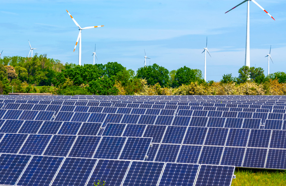 Solar panels and wind turbines in a green landscape under a clear sky.