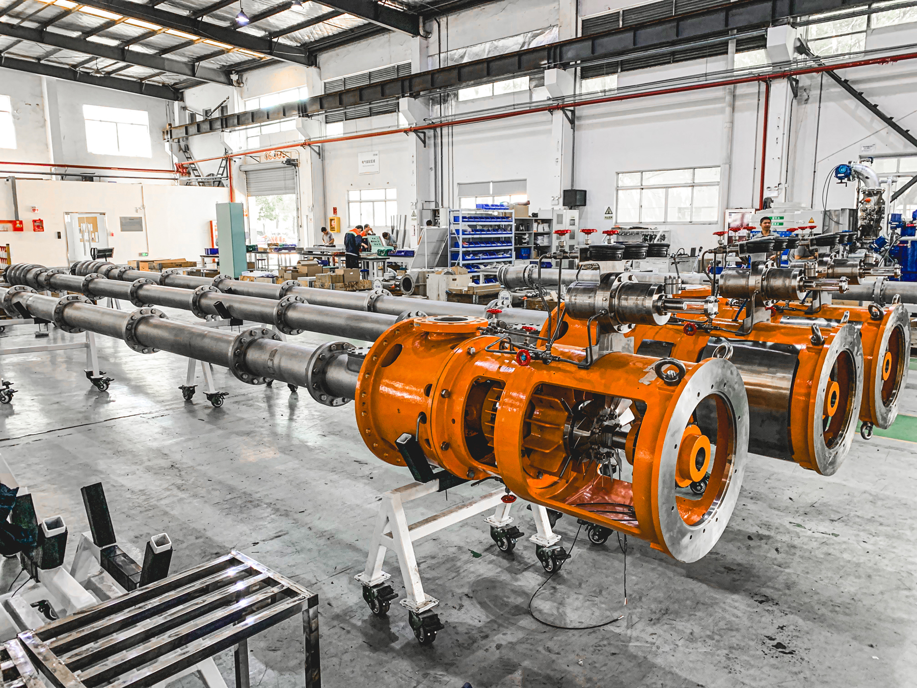 Industriel samlebånd med store orange pumper, sandsynligvis til væskehåndtering.